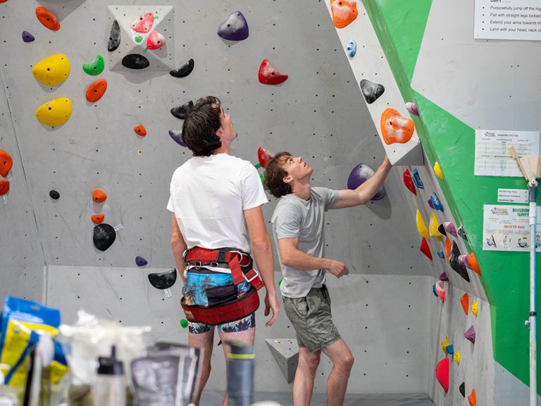Indoor Climb South Coast: climbers considering route on bouldering wall.